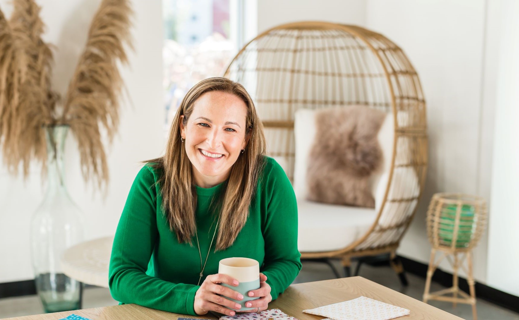 Website owner wearing a green shirt sitting at a table smiling and holding a coffee cup